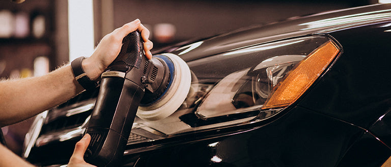 Person using a car polisher on a black car's headlight